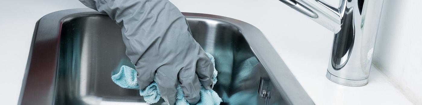 Image of a gloved hand scrubbing a sink clean