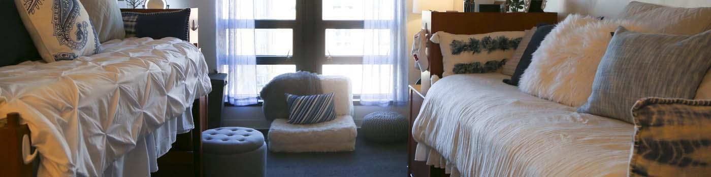 Image of the inside of a dorm room with two beds and seating by the window